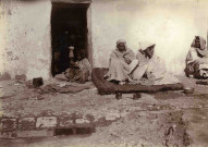 Une jeune fille entrain de piler et des hommes au repos.