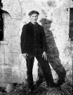 Portrait en pied d'un homme près de la porte d'une étable.