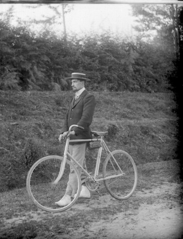 Vélocipédiste au canotier, sur un chemin.