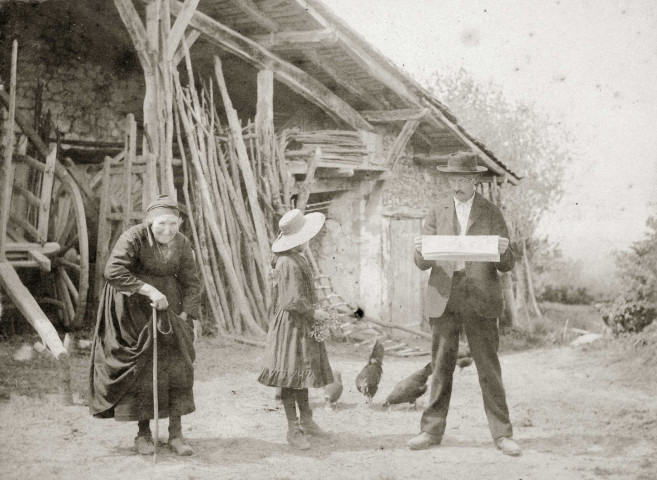 Devant un hangar à bois, jeune fille et couple âgé dont Mathieu Anselme, lisant un journal.
