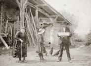 Devant un hangar à bois, jeune fille et couple âgé dont Mathieu Anselme, lisant un journal.
