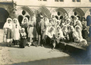 Groupe de jeunes filles en costume traditionnel en compagnie de Louis-Joseph de Bar, le chaptal, dans le cloître.