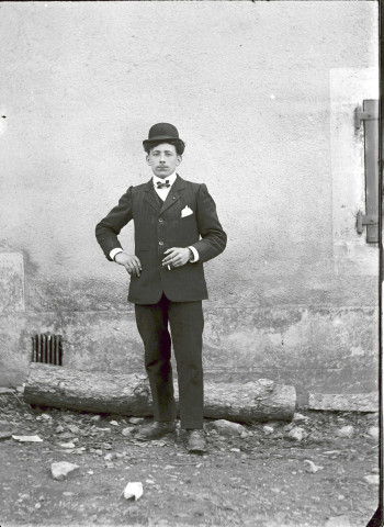 Portrait en pied d'un homme devant le mur d'une maison.