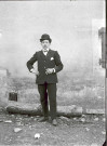 Portrait en pied d'un homme devant le mur d'une maison.