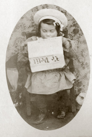 Portrait en pied d'un jeune enfant, assis sur un petit fauteuil, lisant un journal.