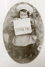 Portrait en pied d'un jeune enfant, assis sur un petit fauteuil, lisant un journal.