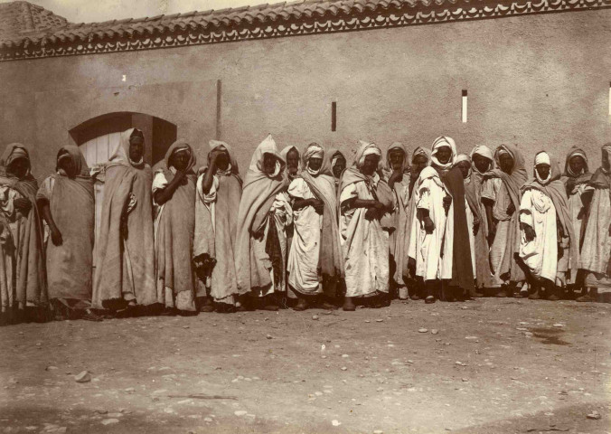 Hommes assis devant la maison du caïd.