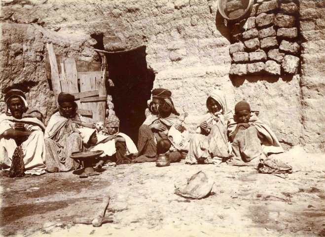 Famille assise devant l'entrée d'une habitation.