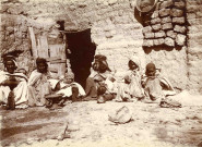 Famille assise devant l'entrée d'une habitation.